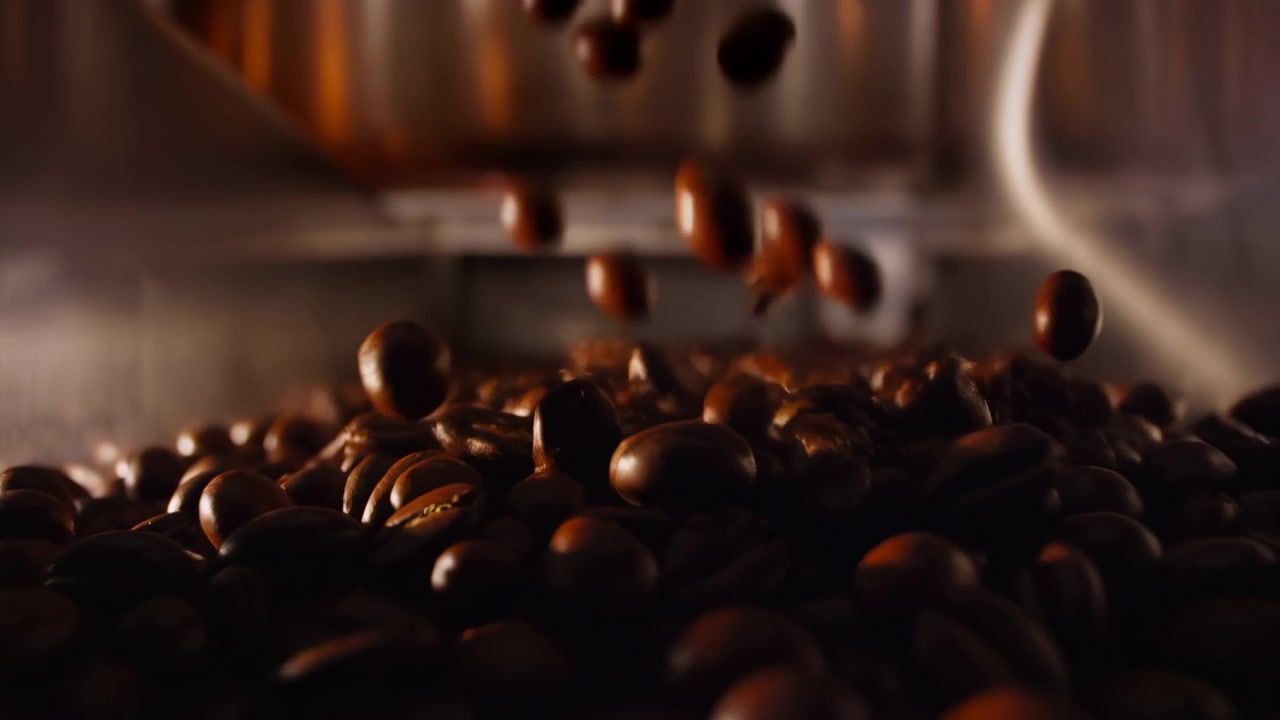 Close-up view shows roasted coffee beans falling into dark heap inside warm metallic chamber, with several beans suspended above pile, creating rich texture, motion, and artisanal food mood