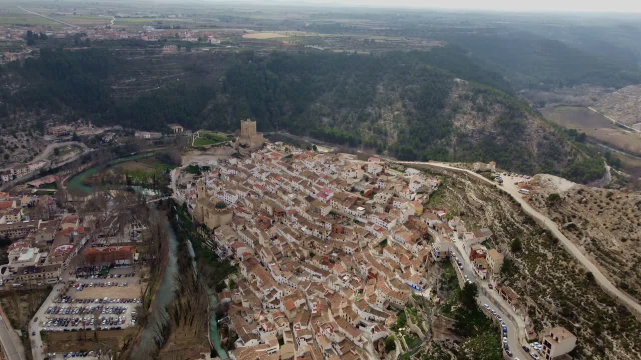 Toma aérea 4K con dron de Alcalá del Júcar, un impresionante pueblo histórico construido en la ladera de un cañón. Presenta el castillo medieval, casas blancas tradicionales y el río Júcar en España.