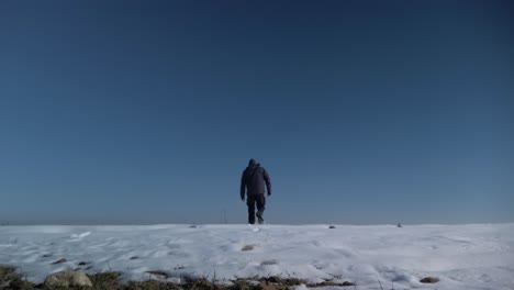 A-tripod-shot-of-a-man-walking-away-in-the-snow-under-a-clear-sky