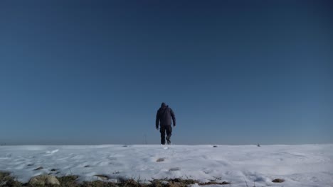 Eine-Stativaufnahme-Eines-Mannes,-Der-Unter-Klarem-Himmel-Im-Schnee-Davonläuft