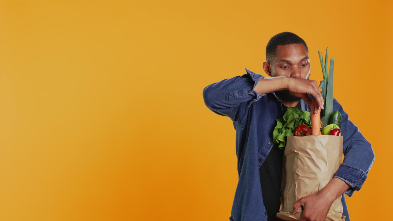 Adulto vegano che presenta una carota matura dalla sua borsa di carta della spesa