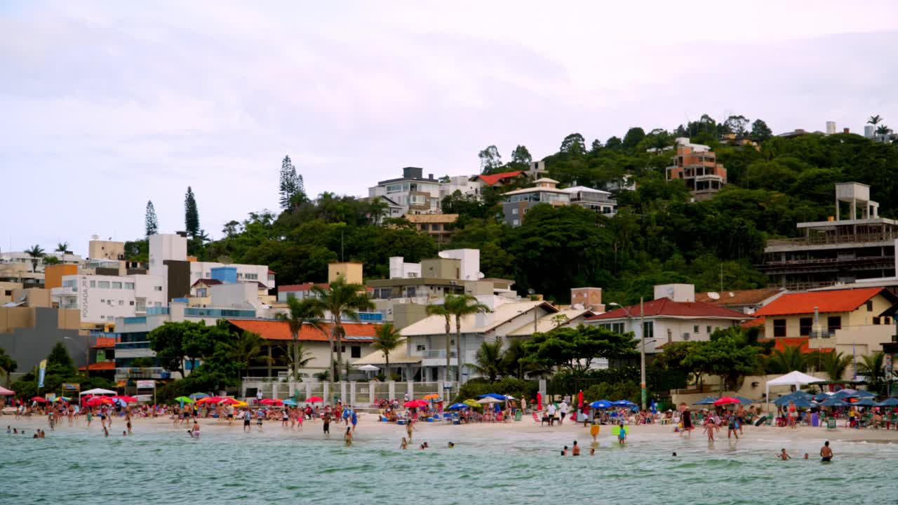 Carrellata a sinistra di persone che si godono l'estate nella zona delle spiagge di Bombas e Bombinhas in Brasile.