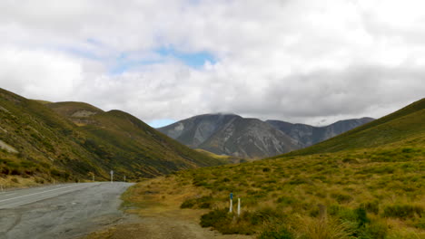 Slow-pan-shot-of-road-following-gigantic-hilly-mountain-landscape-with-cloudscape-at-sky