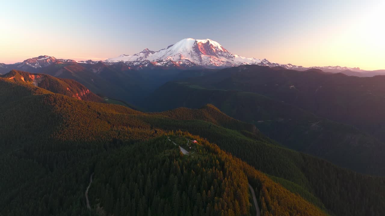 Drone shot of Mount Rainier surrounded by forests in the glow of the sunset