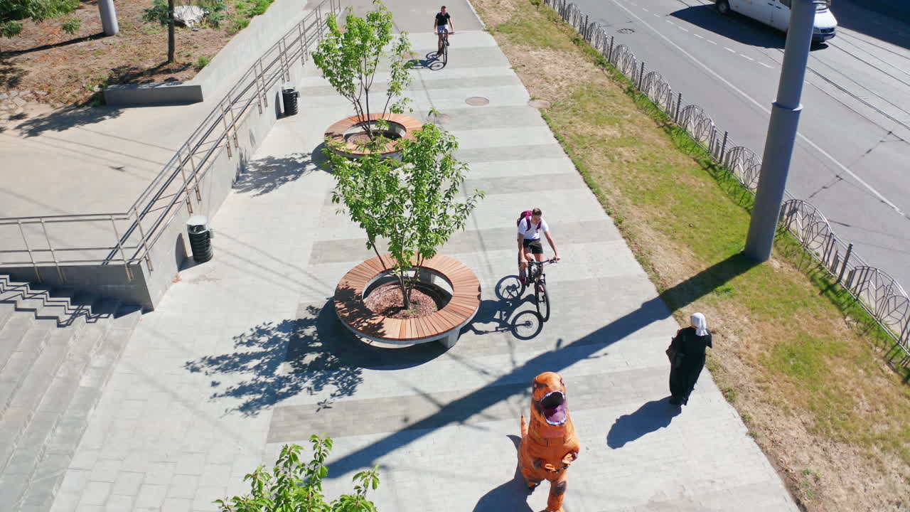 Somebody in funny costume of dinosaur walking along the street. Orange and brown animal suit from aerial perspective.