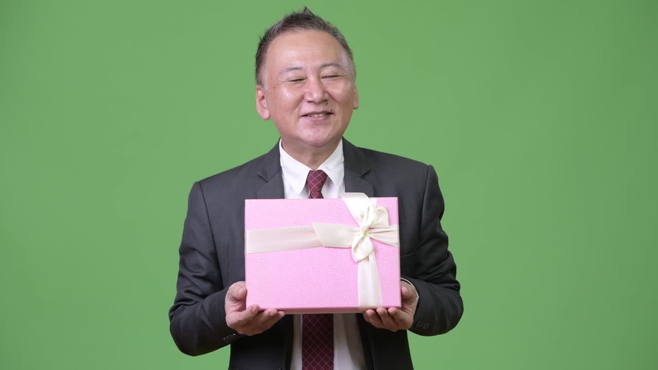 초록색 배경 에 선물 상자 를 가진 성숙 한 일본인 사업가