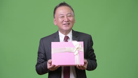 mature japanese businessman with gift box against green background