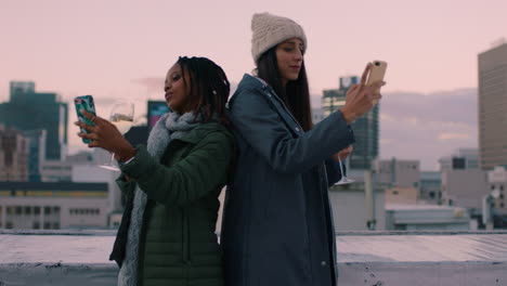 beautiful young women friends taking selfies using smartphone enjoying mobile camera technology hanging out on rooftop at sunset drinking wine