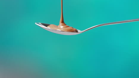 close up of melted chocolate being poured onto spoon and overflowing against blue coloured background with copy space 1