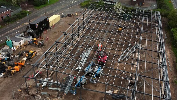 Aufsteigende Luftaufnahme über die Fundament-Stahlkonstruktion und die Bauausrüstung einer Aldi-Supermarkt-Baustelle.