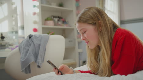 Teenage-girl-wearing-orthodontic-braces-lying-on-bed-at-home-using-mobile-phone-and-smiling---shot-in-slow-motion