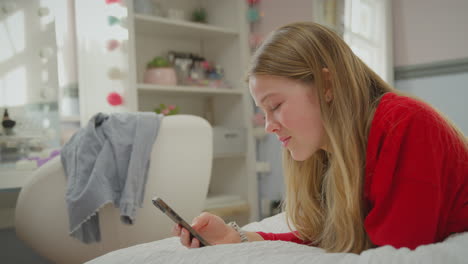teenage girl wearing orthodontic braces lying on bed at home using mobile phone and smiling - shot in slow motion