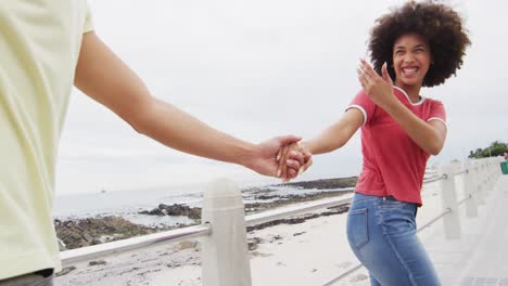 Afroamerikanische-Junge-Frau-Hält-Die-Hände-Ihres-Mannes,-Während-Sie-Auf-Der-Promenade-Spaziert