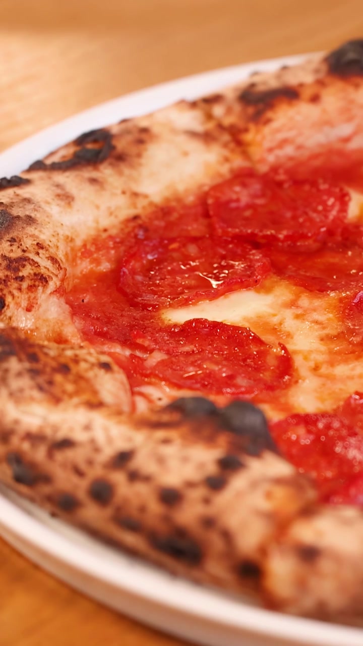 Delle mani posano una pizza napoletana calda con salame piccante e formaggio fuso su un tavolo di legno.