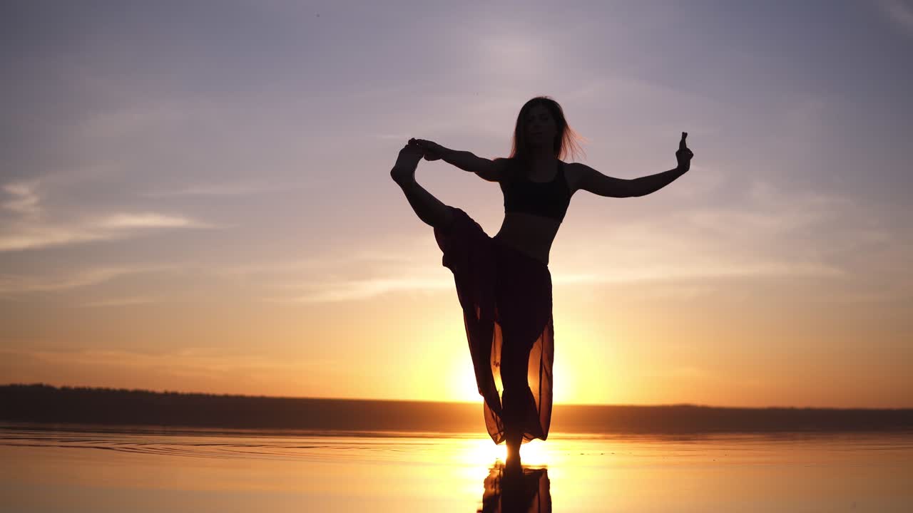 Silhouette yoga woman practicing yoga posture on sea coast at beautiful sunset. Stunning view of a woman in yogi pants. Front view