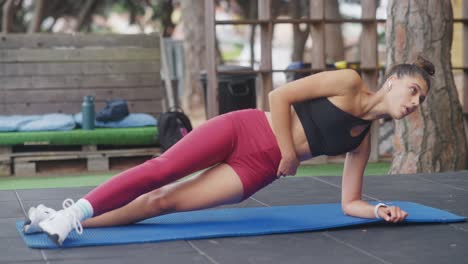 a woman performs a side plank exercise on a mat outdoors