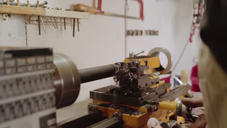 Instrument-maker-forming-block-of-black-grenadilla-wood-using-an-old-dusty-turning-lathe