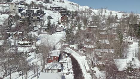 Vista-De-Pájaro-De-Cerca-Que-Establece-El-Pueblo-De-Montaña-Lleno-De-Nieve-De-Farellones-Chile-En-Un-Día-Soleado,-Cabañas-Hechas-De-Materiales-Locales