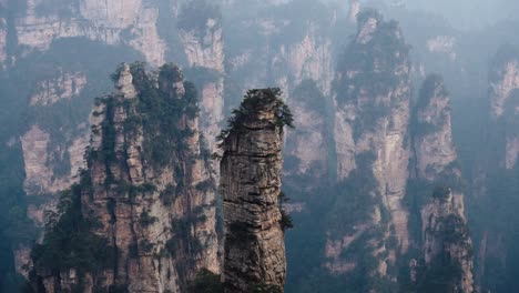 a prominent sandstone spire stands alone among towering cliffs and dense vegetation in zhangjiajie’s unique mountain range