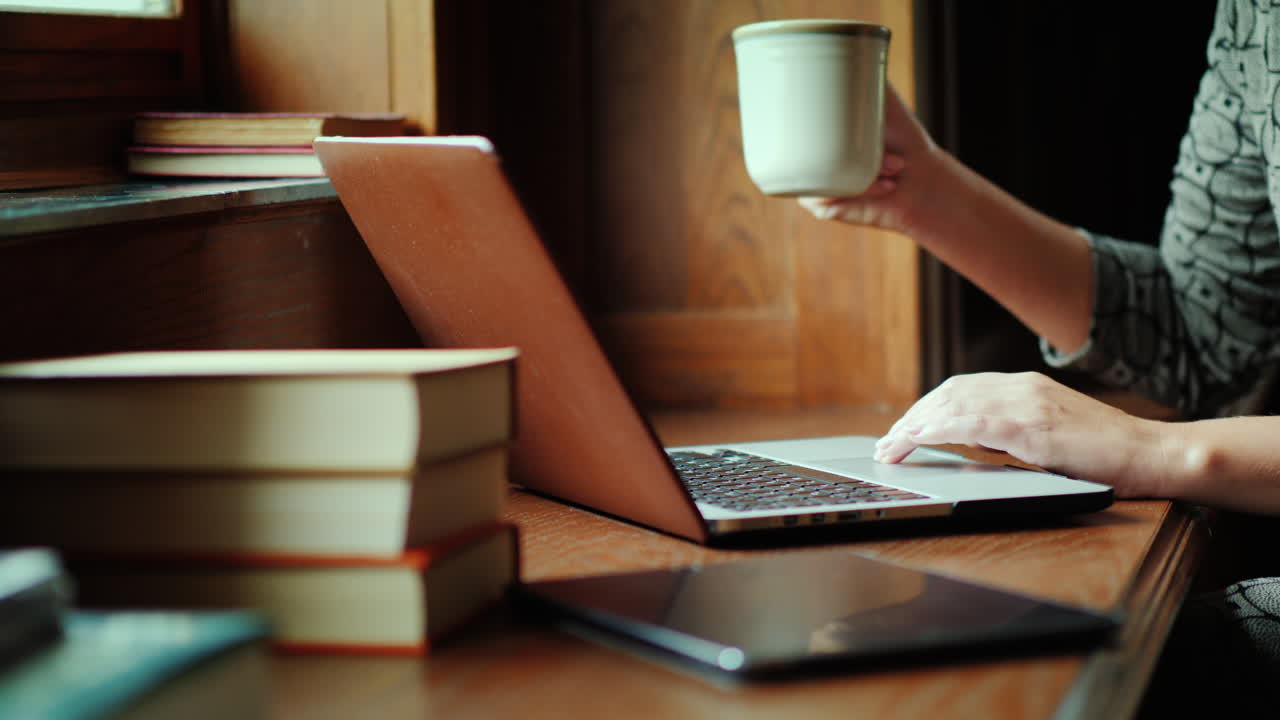 manos escribiendo en la computadora portátil con libros y café
