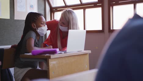 Maestra-Y-Niña-Con-Mascarilla-Usando-Una-Computadora-Portátil-En-Clase-En-La-Escuela