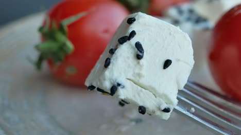 a piece of cheese with black seeds on a fork next to tomatoes