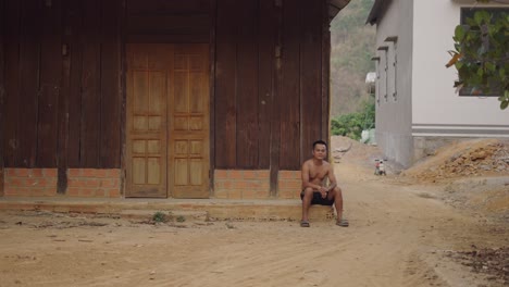 man sitting outside wooden house in rural area