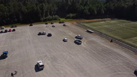 A-white-pick-up-truck-driving-in-circles,-kicking-up-dust-and-making-donuts-at-a-fair-or-festival-event-in-Squamish-BC-from-an-aerial-view-of-the-parking-lot-with-a-4K-drone