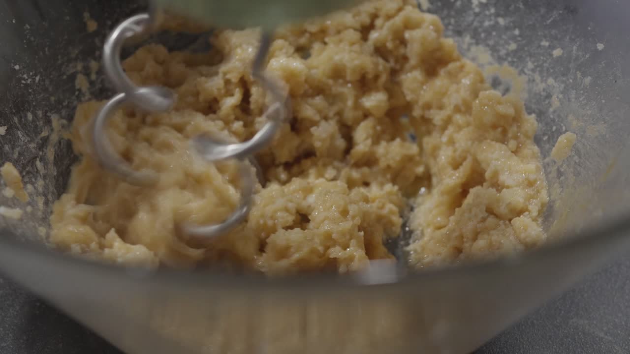 Hand mixer blending cookie dough mixture inside glass bowl during baking