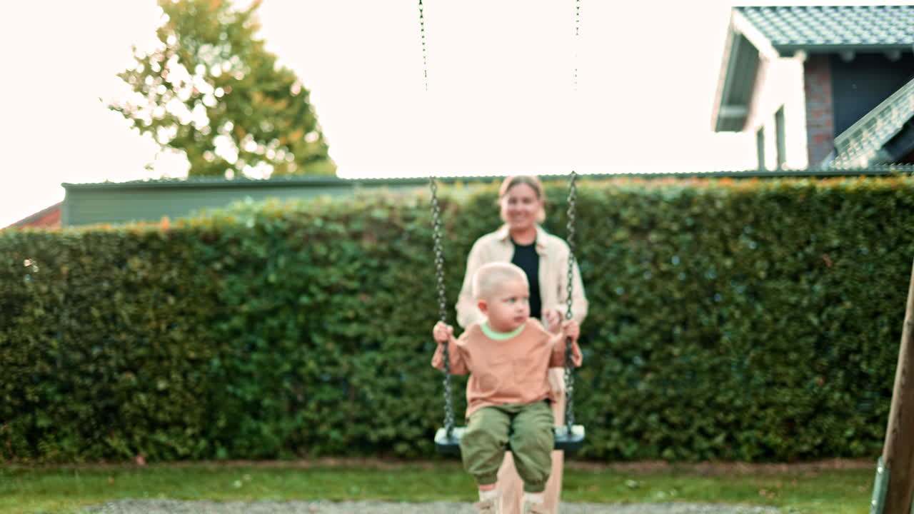 Una mamma allegra fa dondolare il figlio seduto su un'altalena al parco giochi. Madre e figlio si divertono giocando all'aperto. Bambino e madre giocano al parco giochi. Momento della mamma con il suo bambino.