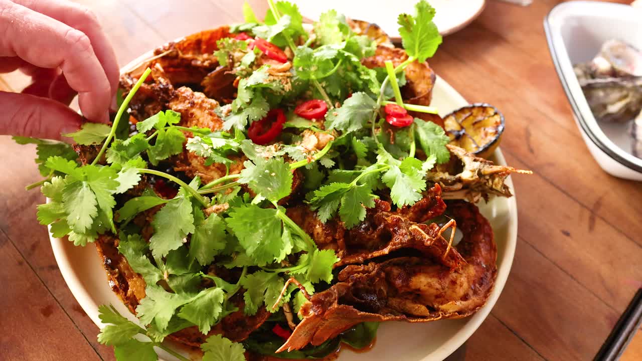Chef garnishes a vibrant lobster dish with fresh herbs and spices under warm lighting on a wooden table
