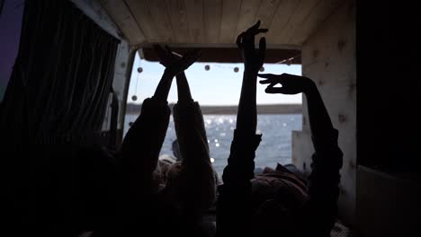 two girls are lying in the back of a caravan by a lake and move their hands sinuously. they have a beautiful view.