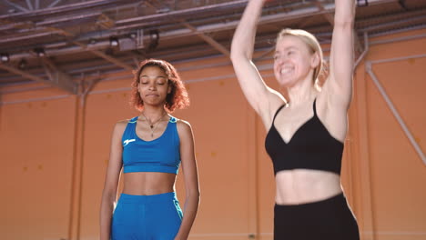 alegre atleta femenina celebrando la victoria mientras su competidora la mira con expresión triste en una instalación deportiva cubierta