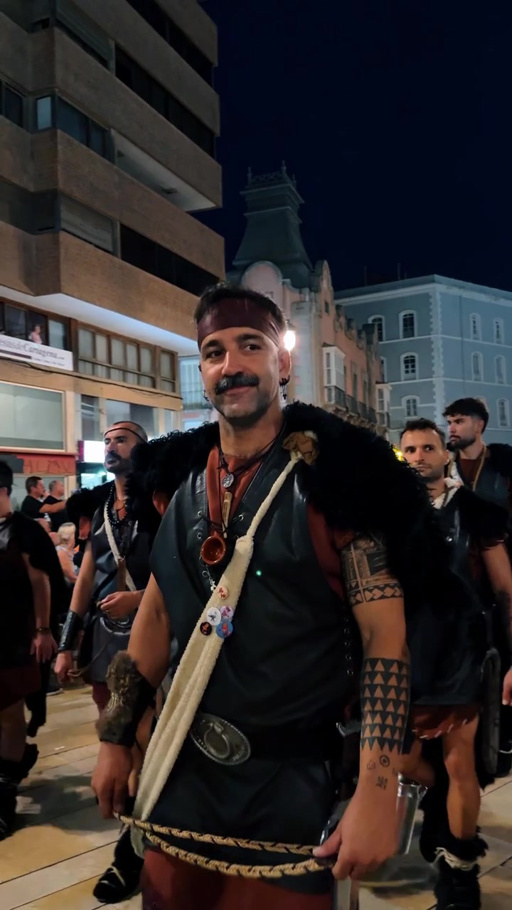 Alicante, Spain, 9 August 2025: Men in warrior costumes with fur capes at parade. Group of men in grey tunics and fur capes marching through city streets during a night historical festival.