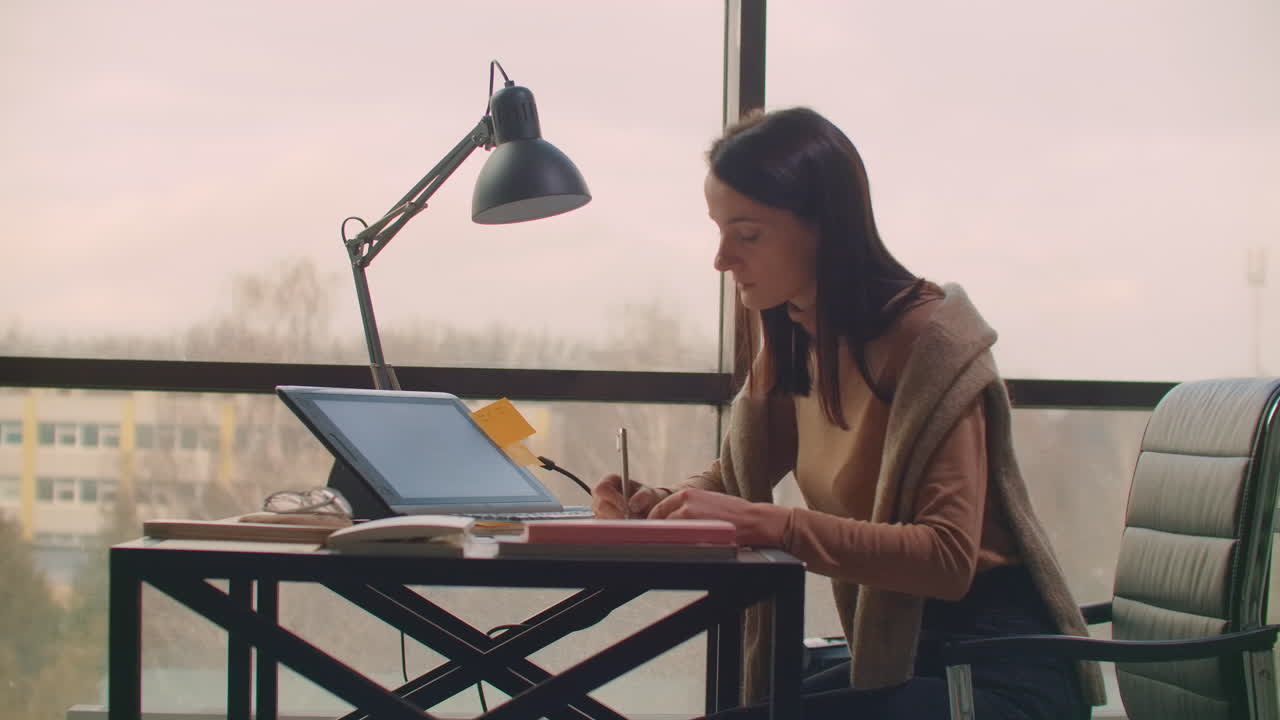 A female graphic designer works in an office with large Windows and paints using a stylus and a computer touch screen. Workstation with touchscreen for designers. Come up with and develop the concept of the logo.
