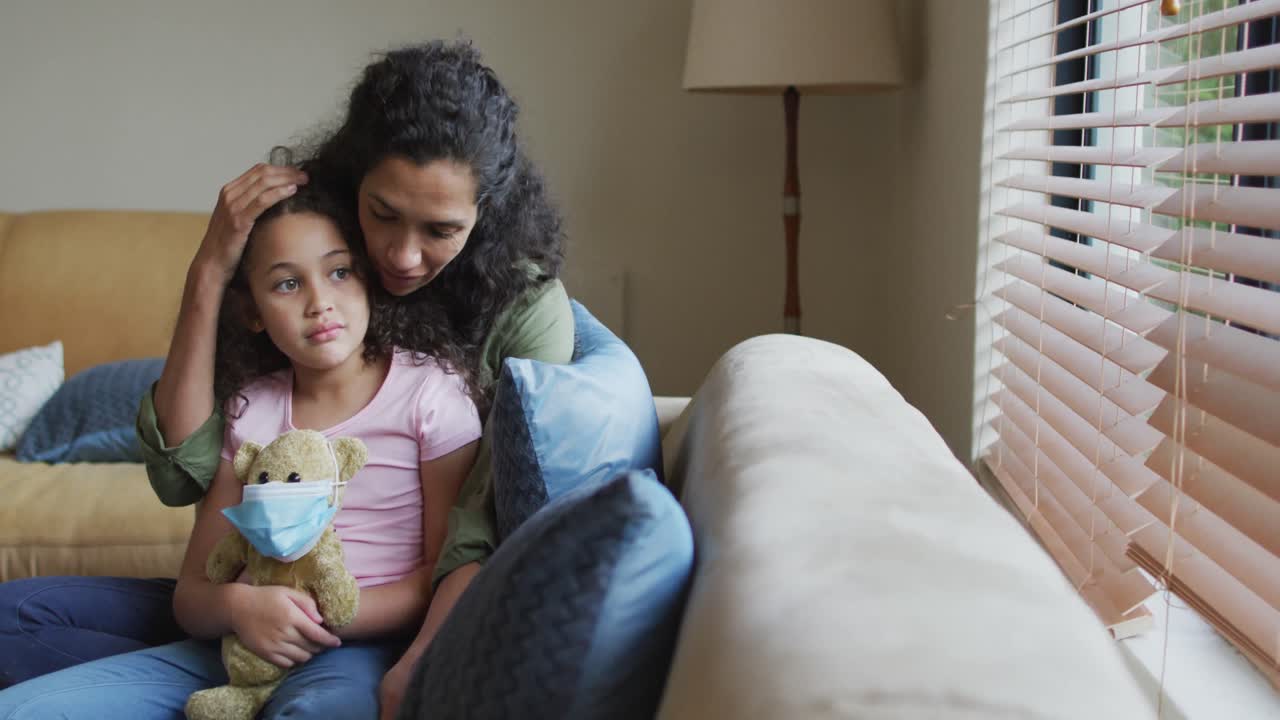 madre e hija de raza mixta abrazándose, hija sosteniendo un oso con máscara facial