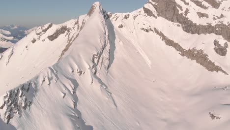 Flying-over-a-large,-snow-covered-mountain-to-look-over-a-mountain-range