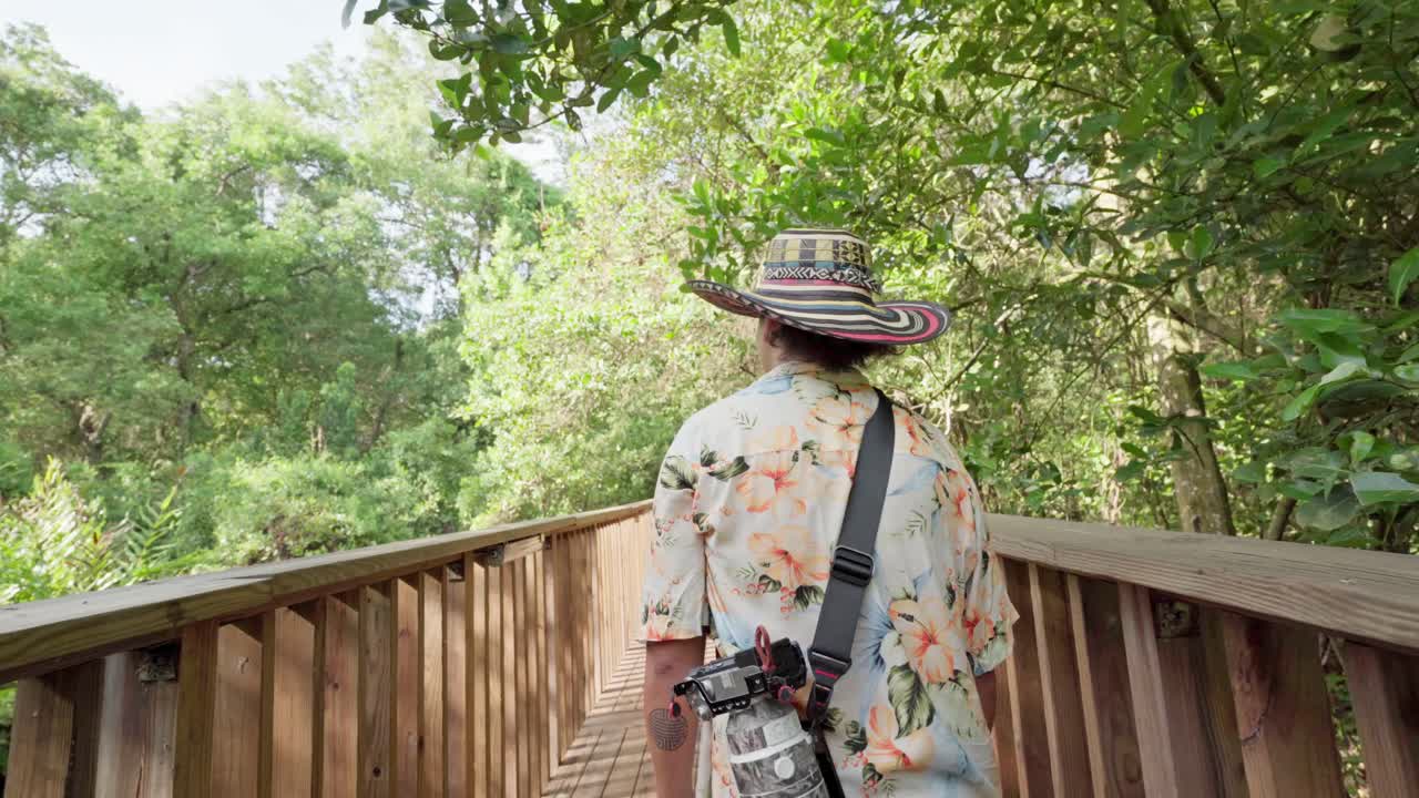 Wildlife photographer walking on a wooden path in a lush green natural park during a sunny day, cienaga de marllorquin, colombia
