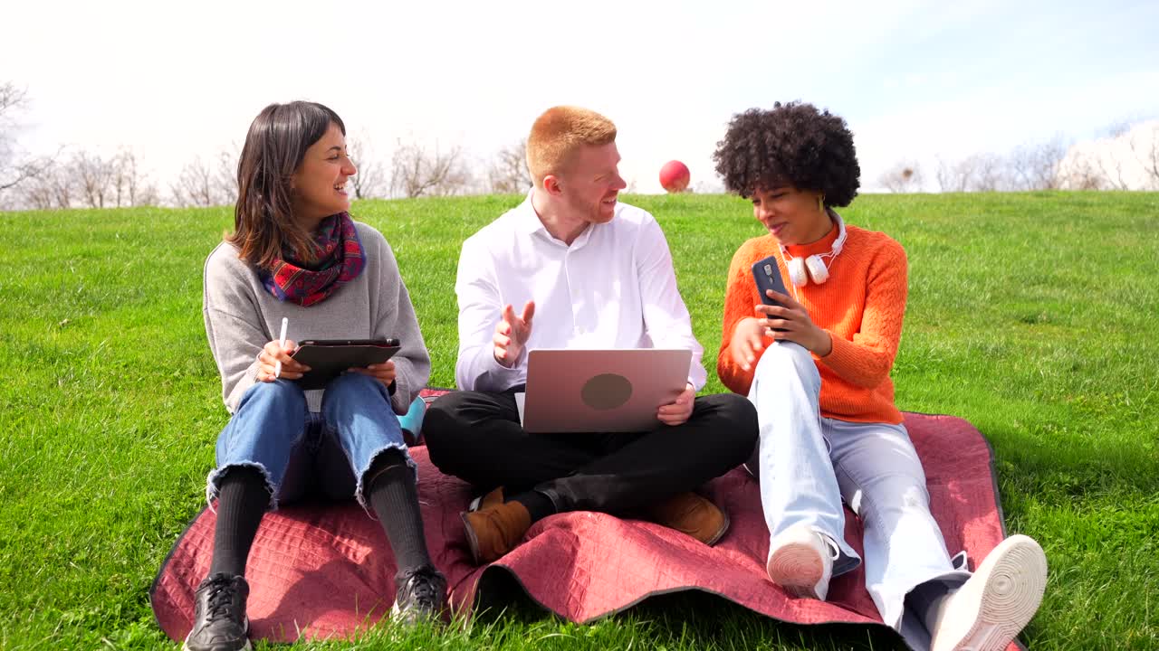Group of people enjoying a picnic in the park with laptops and tablets