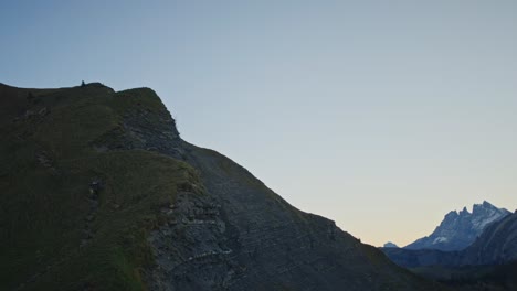 a mountain biking is carrying his bike up a steep and exposed alpine ridge at dawn