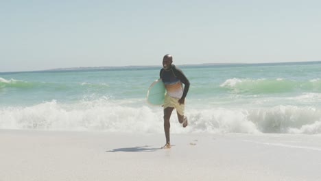 Hombre-Afroamericano-Senior-Corriendo-Con-Tabla-De-Surf-En-La-Playa-Soleada