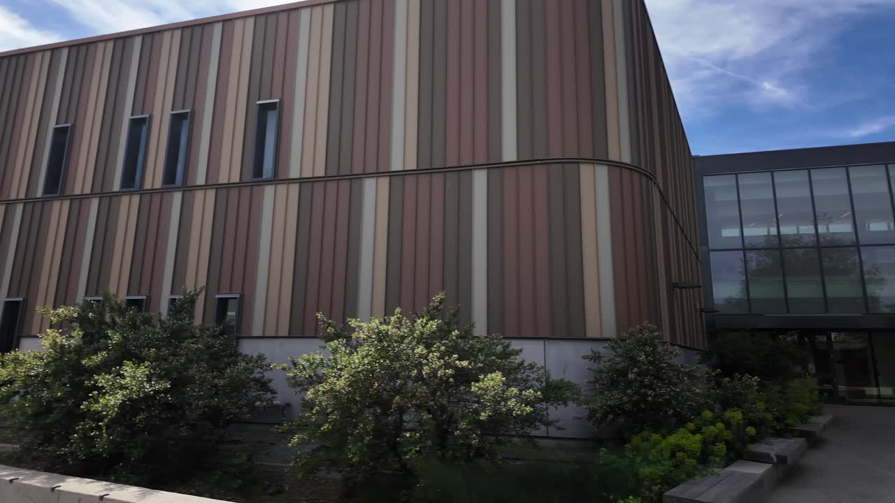 Toma panorámica que revela el diseño arquitectónico contemporáneo del campus de West Valley College, destacando su fachada de rayas multicolores, numerosas ventanas y la entrada ajardinada del patio