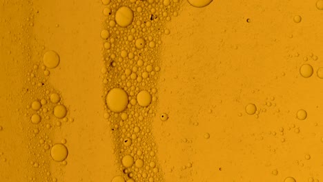 dirty golden oil flow with black spots slowly with bubbles and dust on surface