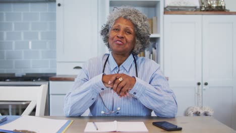 Portrait-of-senior-african-american-female-doctor-talking-while-having-a-videocall-at-home