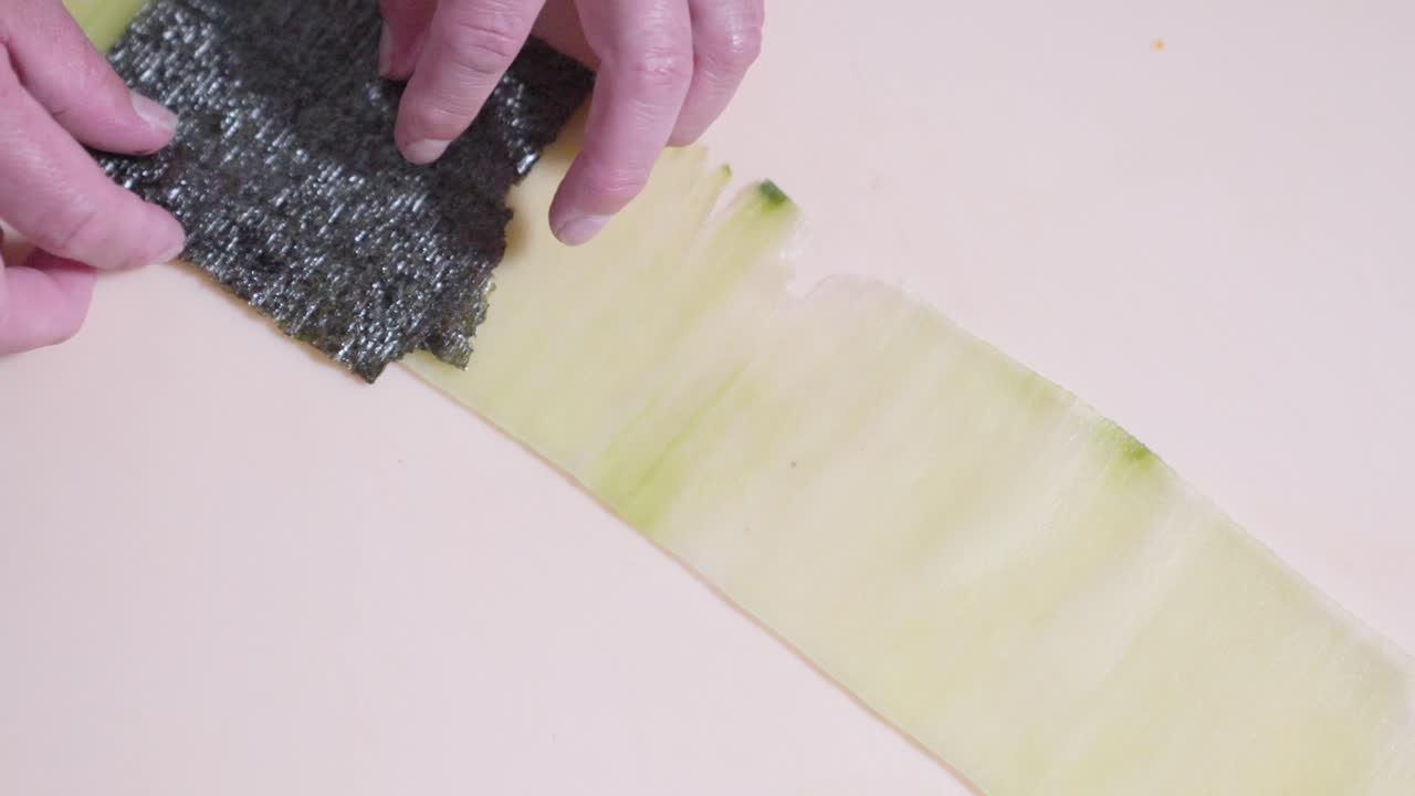 A roaming overhead shot of sushi ingredients being carefully placed on a cucumber slice, showcasing the sushi-making process. Perfect for highlighting fresh ingredients and sushi preparation.