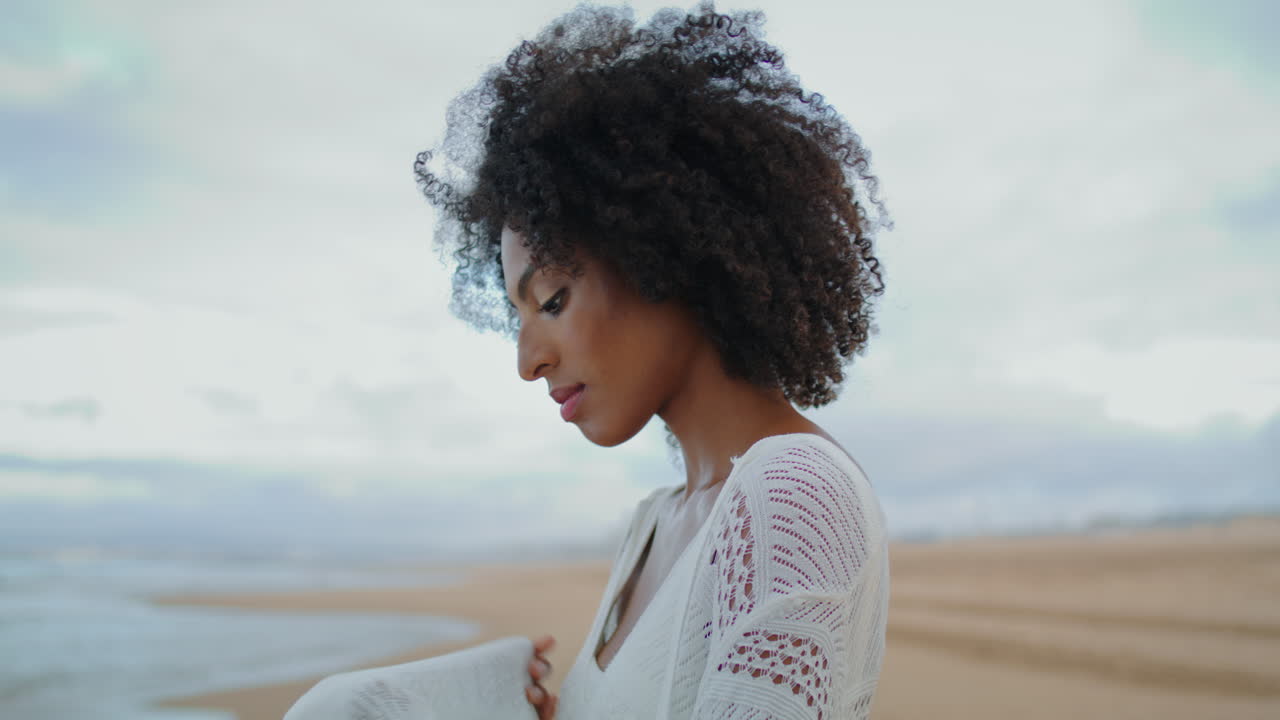 Donna preoccupata in verticale che guarda il mare in una giornata cupa, primo piano. Afroamericana pensierosa.