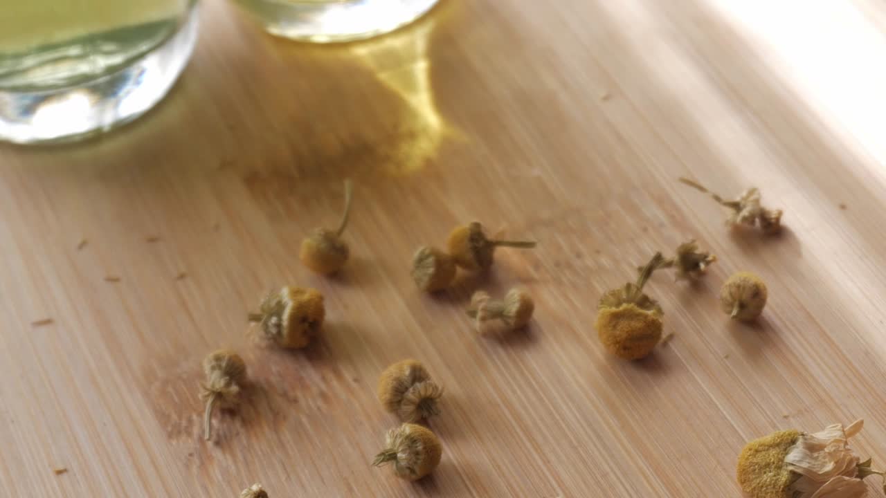 A collection of dried chamomile flowers on a wooden surface, near chamomile liquor
