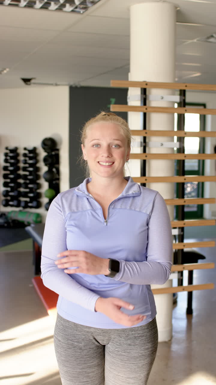 Vertical video: Smiling in gym, woman wearing smartwatch focusing on disability rehabilitation exerc