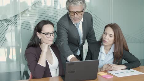 smiling ceo in glasses pointing at laptop and explaining details