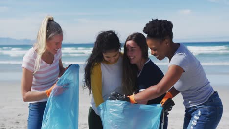 grupo diverso de amigas poniendo basura en bolsas de basura en la playa